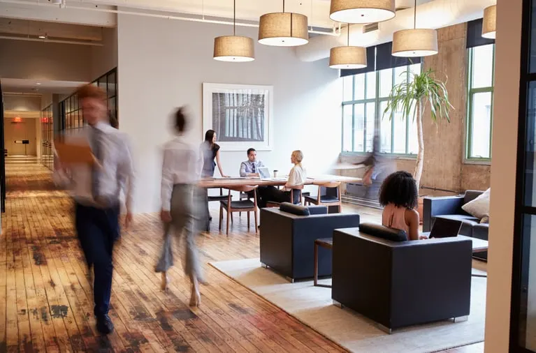 Office workers walking through a modern open-plan office with a meeting table