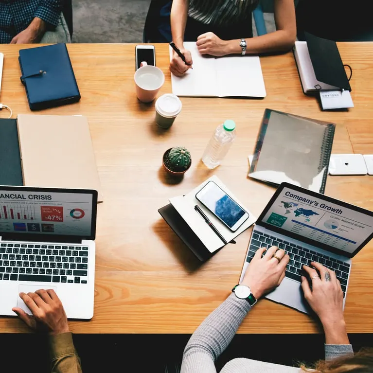 Overhead view of a team meeting table with laptops showing financial and growth charts