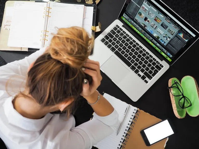 Stressed woman with head in hands at a desk with an open laptop and notebook