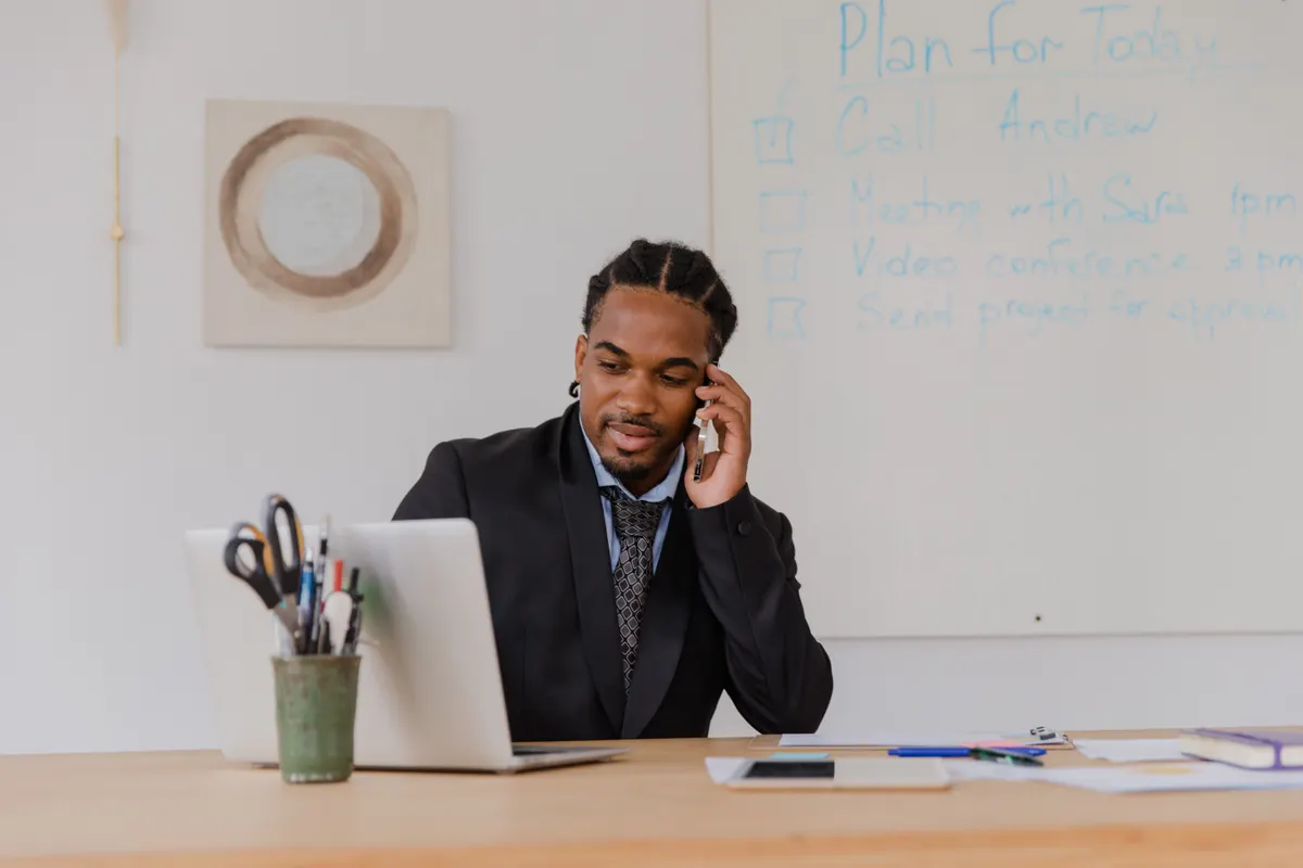 Businessman on the phone at his desk with a planning whiteboard behind him