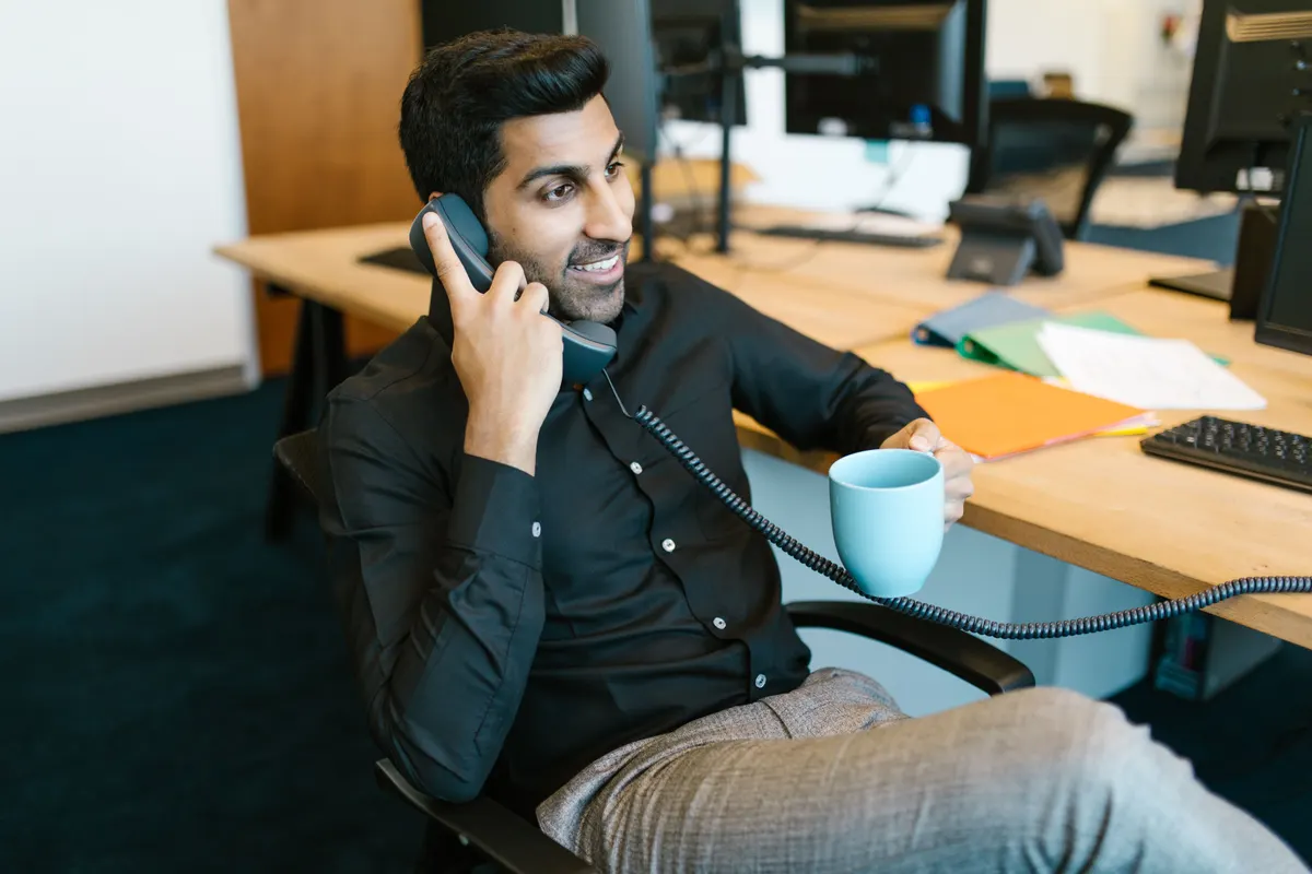 Man on the phone gesturing at his desk in front of a monitor