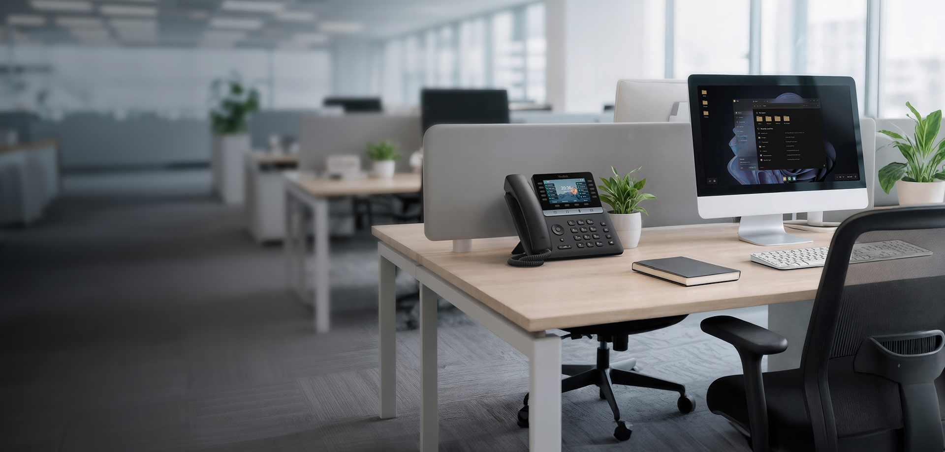 Business IP desk phone and monitor on a desk in a modern open-plan office